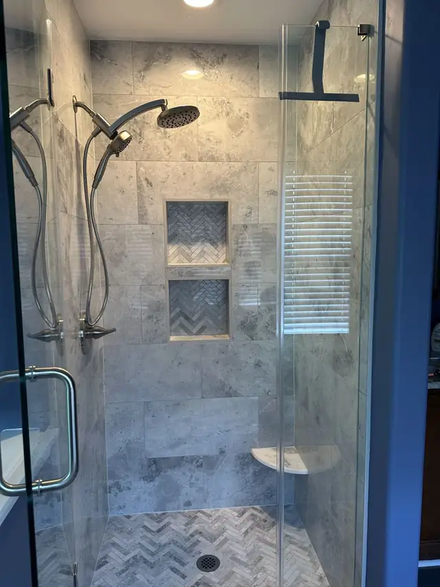 Marble tile shower with two recessed niches lined in herringbone tile and dual shower heads