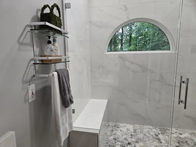 Marble-look walk-in shower with an arched window, glass door, built-in bench and pebble floor