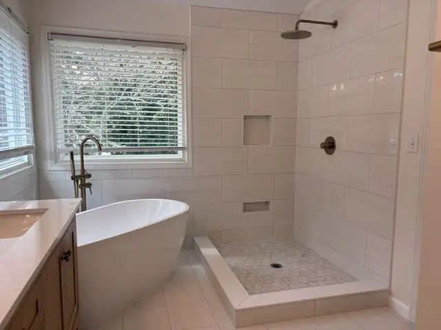 Freestanding white tub beside a walk-in tile shower with a matte black rain head and mosaic floor