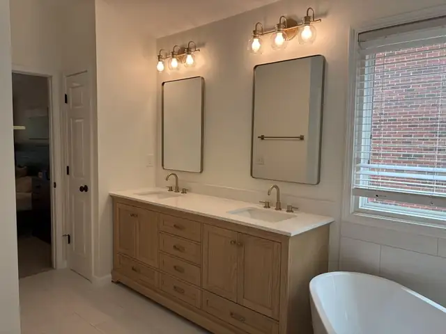 Light wood double vanity with a white top, two framed mirrors and brass wall lights